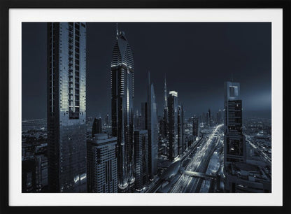 A framed, blue-toned nighttime photograph of a futuristic city skyline from an elevated perspective, featuring illuminated skyscrapers and light trails from traffic on a major highway stretching into the distance. Poster