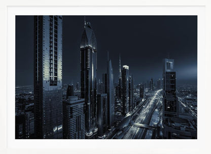 A framed, blue-toned nighttime photograph of a futuristic city skyline from an elevated perspective, featuring illuminated skyscrapers and light trails from traffic on a major highway stretching into the distance. Poster