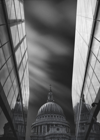 A dramatic black and white, low-angle photograph of St. Paul's Cathedral in London, framed between two modern, reflective glass skyscrapers. A long exposure effect blurs the clouds in the sky, creating streaks of light and shadow behind the cathedral's dome. Poster