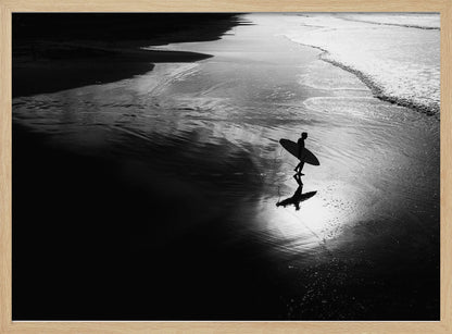 A high-contrast, black and white photograph of a silhouetted surfer carrying a surfboard and walking along the wet, reflective sand at the water's edge. Decor