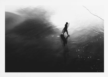 A high-contrast, black and white photograph of a surfer silhouetted against the bright reflection of the sun on the water. The surfer is carrying a surfboard and walking along the wet sand, leaving footprints behind. Their long shadow is cast in front of them on the dark, glistening sand. Print