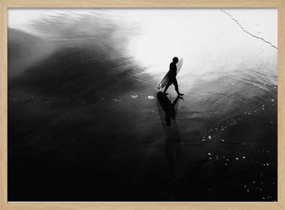 A high-contrast, black and white photograph of a surfer silhouetted against the bright reflection of the sun on the water. The surfer is carrying a surfboard and walking along the wet sand, leaving footprints behind. Their long shadow is cast in front of them on the dark, glistening sand. Print