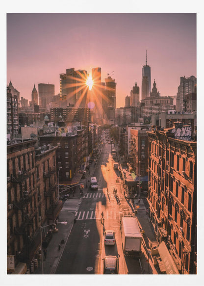 A high-angle view of a New York City street at sunset, with the sun bursting between skyscrapers and casting long golden shadows over the buildings and traffic below. Decor