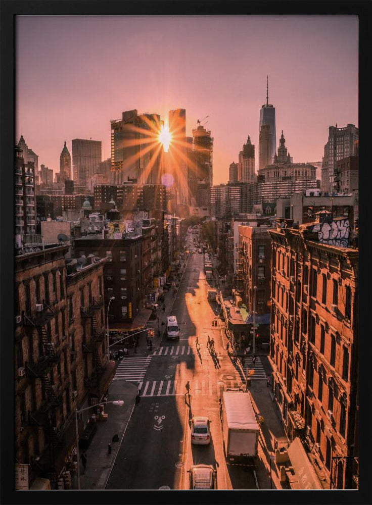 A high-angle view of a New York City street at sunset, with the sun bursting between skyscrapers and casting long golden shadows over the buildings and traffic below. Decor