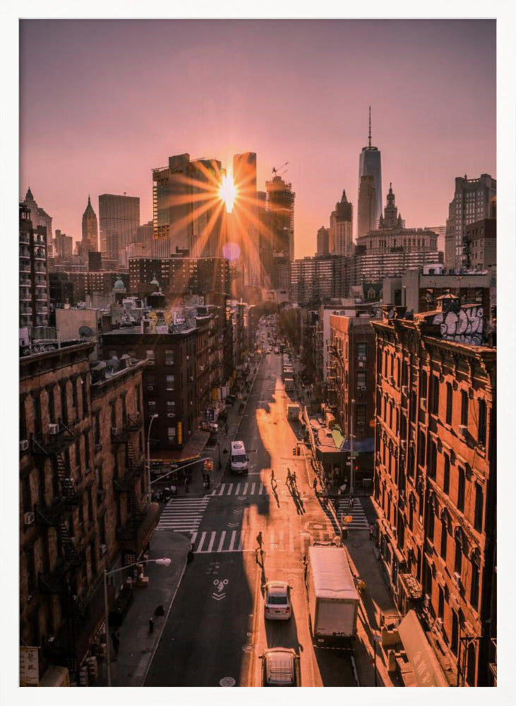 A high-angle view of a New York City street at sunset, with the sun bursting between skyscrapers and casting long golden shadows over the buildings and traffic below. Decor