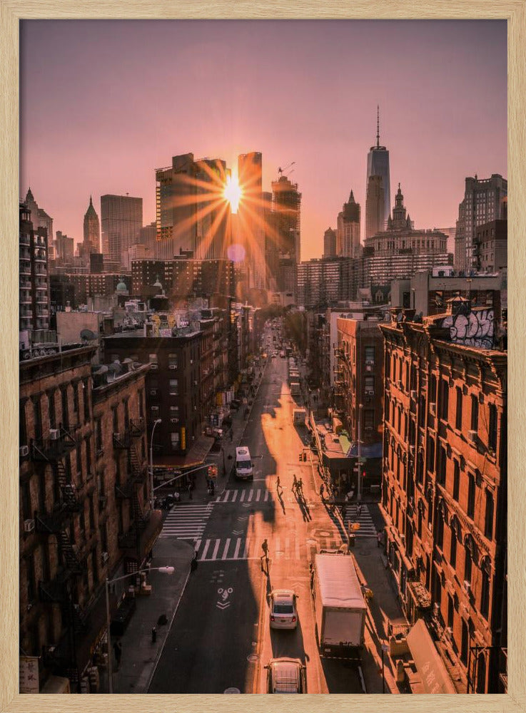 A high-angle view of a New York City street at sunset, with the sun bursting between skyscrapers and casting long golden shadows over the buildings and traffic below. Decor