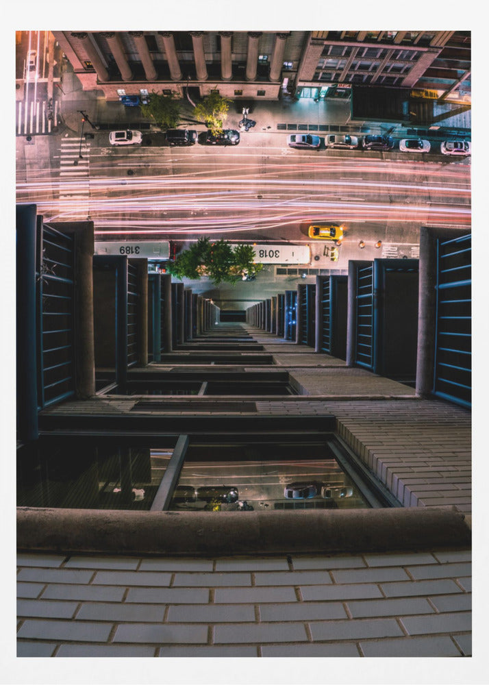 A dizzying bird's-eye view looking straight down the side of a skyscraper into a busy city street at night, with long exposure light trails from traffic creating streaks of red and white below. Wall Art