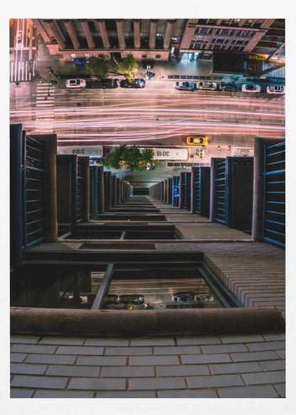 A dizzying bird's-eye view looking straight down the side of a skyscraper into a busy city street at night, with long exposure light trails from traffic creating streaks of red and white below. Wall Art