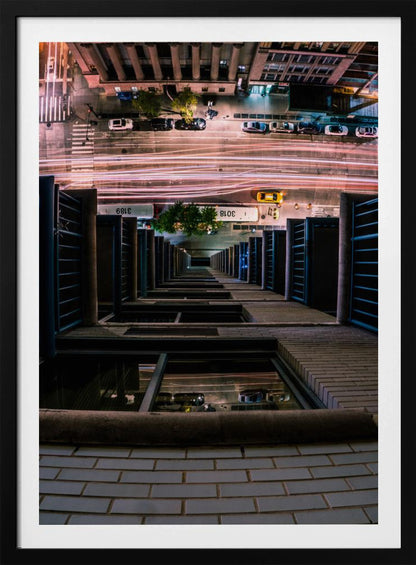 A dizzying bird's-eye view looking straight down the side of a skyscraper into a busy city street at night, with long exposure light trails from traffic creating streaks of red and white below. Wall Art