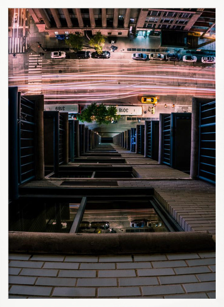 A dizzying bird's-eye view looking straight down the side of a skyscraper into a busy city street at night, with long exposure light trails from traffic creating streaks of red and white below. Wall Art