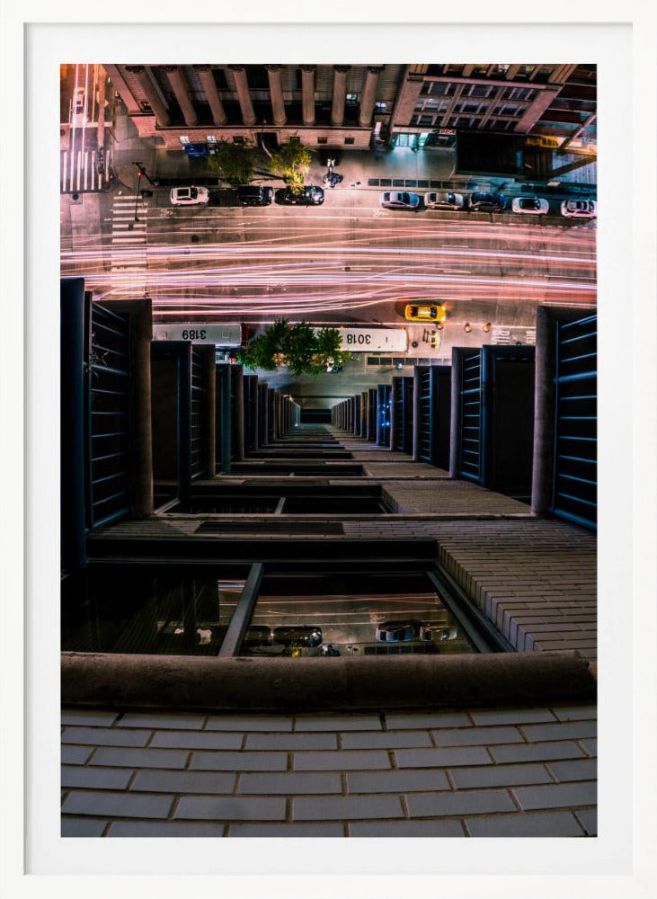 A dizzying bird's-eye view looking straight down the side of a skyscraper into a busy city street at night, with long exposure light trails from traffic creating streaks of red and white below. Wall Art