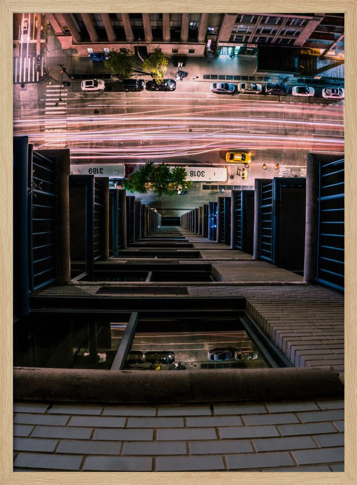 A dizzying bird's-eye view looking straight down the side of a skyscraper into a busy city street at night, with long exposure light trails from traffic creating streaks of red and white below. Wall Art