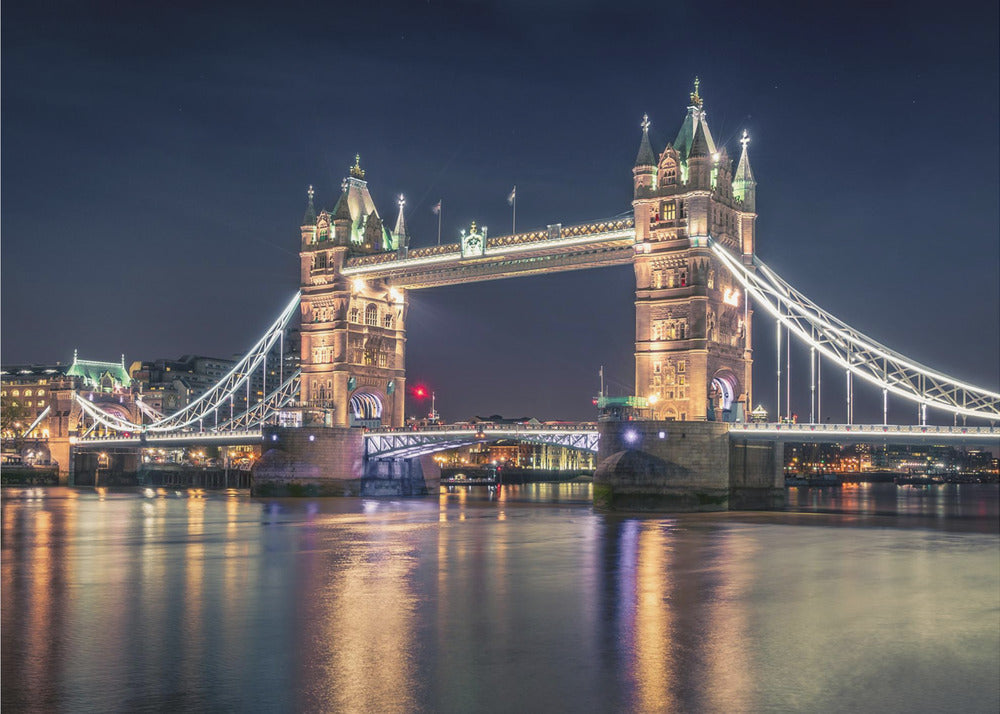 A stunning night photograph of London's iconic Tower Bridge, fully illuminated with golden and white lights that cast a shimmering reflection on the dark waters of the River Thames below, all set against a deep night sky and enclosed in a silver frame. Poster