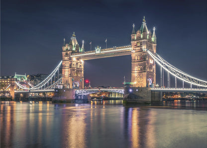 A stunning night photograph of London's iconic Tower Bridge, fully illuminated with golden and white lights that cast a shimmering reflection on the dark waters of the River Thames below, all set against a deep night sky and enclosed in a silver frame. Poster