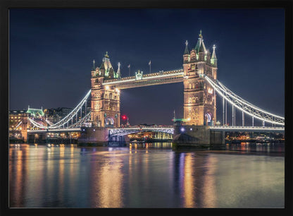 A stunning night photograph of London's iconic Tower Bridge, fully illuminated with golden and white lights that cast a shimmering reflection on the dark waters of the River Thames below, all set against a deep night sky and enclosed in a silver frame. Poster