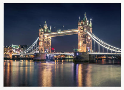 A stunning night photograph of London's iconic Tower Bridge, fully illuminated with golden and white lights that cast a shimmering reflection on the dark waters of the River Thames below, all set against a deep night sky and enclosed in a silver frame. Poster
