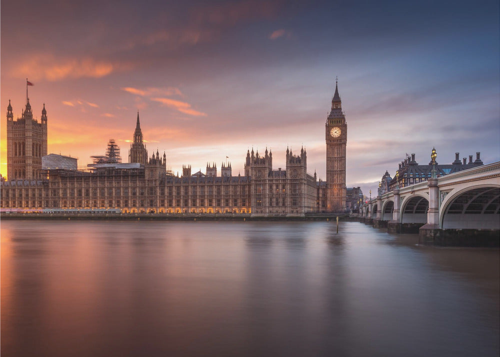 A framed photograph of the Houses of Parliament and Big Ben in London at sunset, with a dramatic orange and purple sky reflecting in the calm waters of the River Thames. Artwork