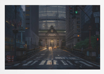 A moody photograph of a wet city street at dusk, leading towards the illuminated facade of Grand Central Terminal in New York City, which is framed by tall, modern skyscrapers. Decor