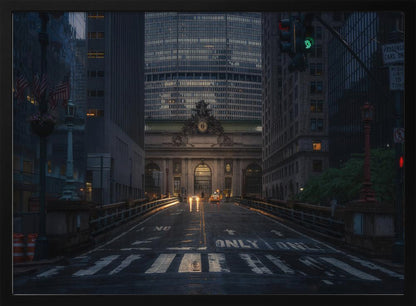 A moody photograph of a wet city street at dusk, leading towards the illuminated facade of Grand Central Terminal in New York City, which is framed by tall, modern skyscrapers. Decor