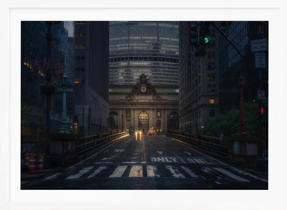 A moody photograph of a wet city street at dusk, leading towards the illuminated facade of Grand Central Terminal in New York City, which is framed by tall, modern skyscrapers. Decor