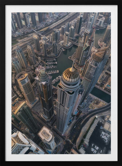 An aerial, bird's-eye view of the dense Dubai Marina, with towering skyscrapers casting long shadows. A waterway snakes through the urban canyon, with numerous yachts docked in the marina. A prominent skyscraper with a distinctive golden dome stands in the foreground. Artwork