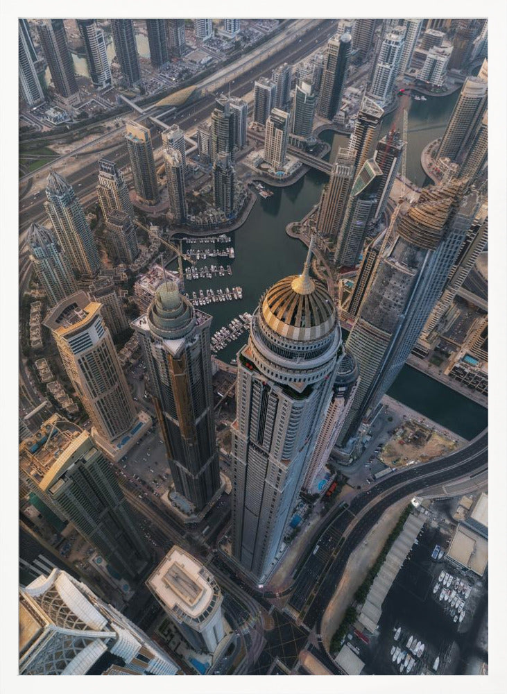An aerial, bird's-eye view of the dense Dubai Marina, with towering skyscrapers casting long shadows. A waterway snakes through the urban canyon, with numerous yachts docked in the marina. A prominent skyscraper with a distinctive golden dome stands in the foreground. Artwork