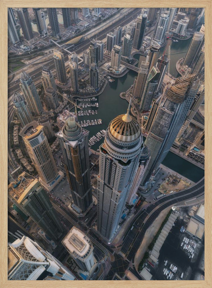 An aerial, bird's-eye view of the dense Dubai Marina, with towering skyscrapers casting long shadows. A waterway snakes through the urban canyon, with numerous yachts docked in the marina. A prominent skyscraper with a distinctive golden dome stands in the foreground. Artwork