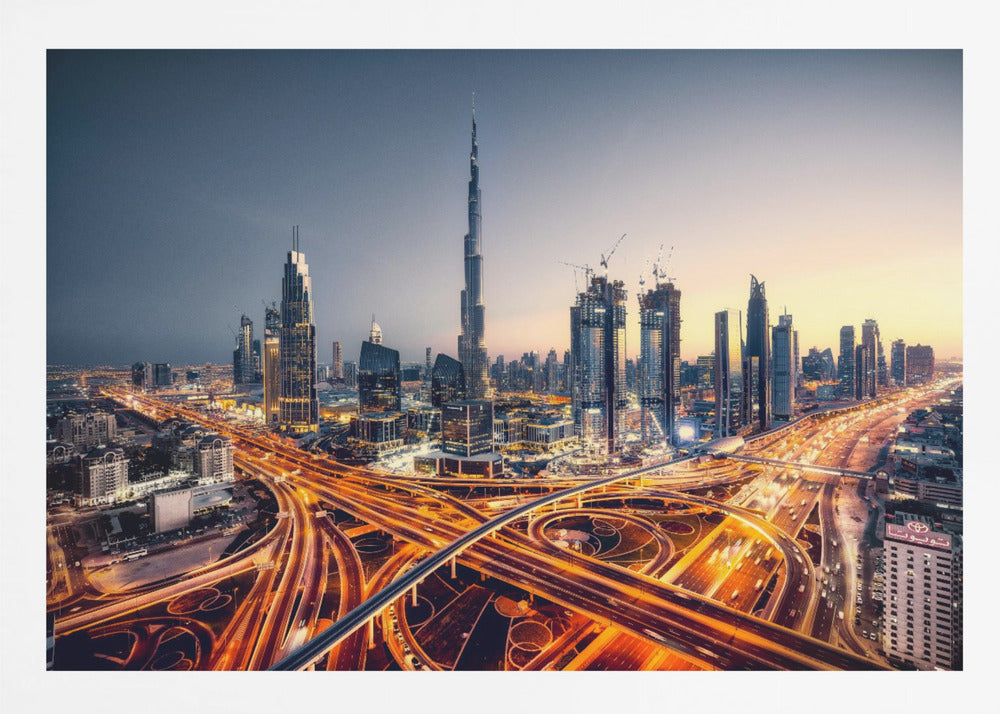 A wide-angle, elevated photograph of the Dubai skyline at dusk, with the iconic Burj Khalifa towering in the center. In the foreground, a complex network of highways glows with the orange light trails of moving traffic, while the city's numerous skyscrapers are illuminated against a twilight sky. Print