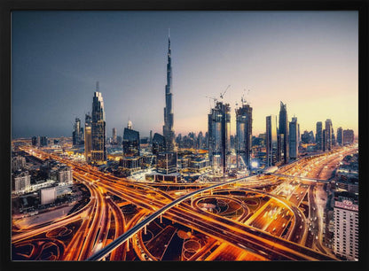 A wide-angle, elevated photograph of the Dubai skyline at dusk, with the iconic Burj Khalifa towering in the center. In the foreground, a complex network of highways glows with the orange light trails of moving traffic, while the city's numerous skyscrapers are illuminated against a twilight sky. Print