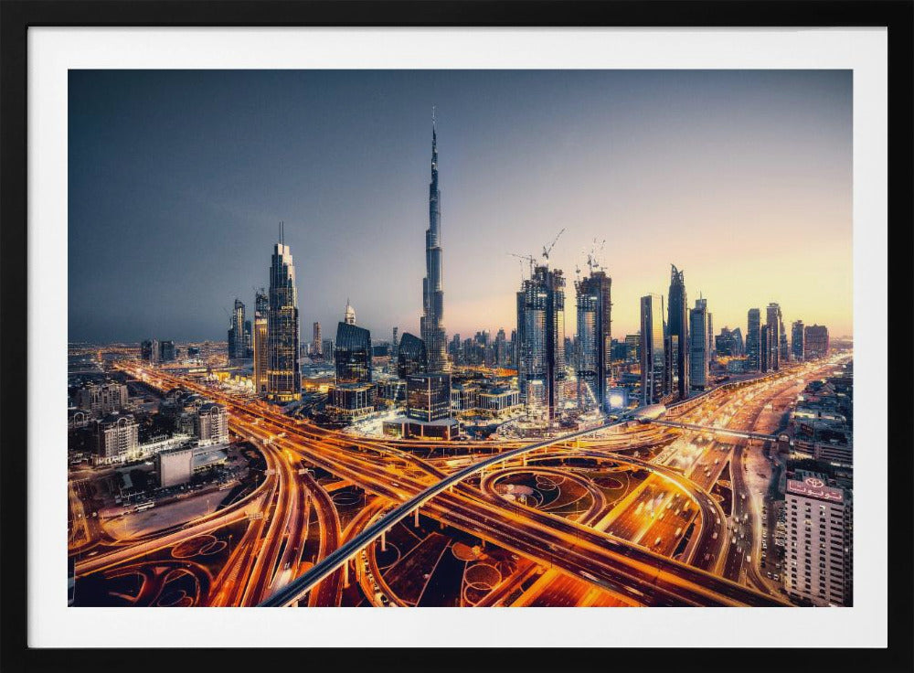 A wide-angle, elevated photograph of the Dubai skyline at dusk, with the iconic Burj Khalifa towering in the center. In the foreground, a complex network of highways glows with the orange light trails of moving traffic, while the city's numerous skyscrapers are illuminated against a twilight sky. Print