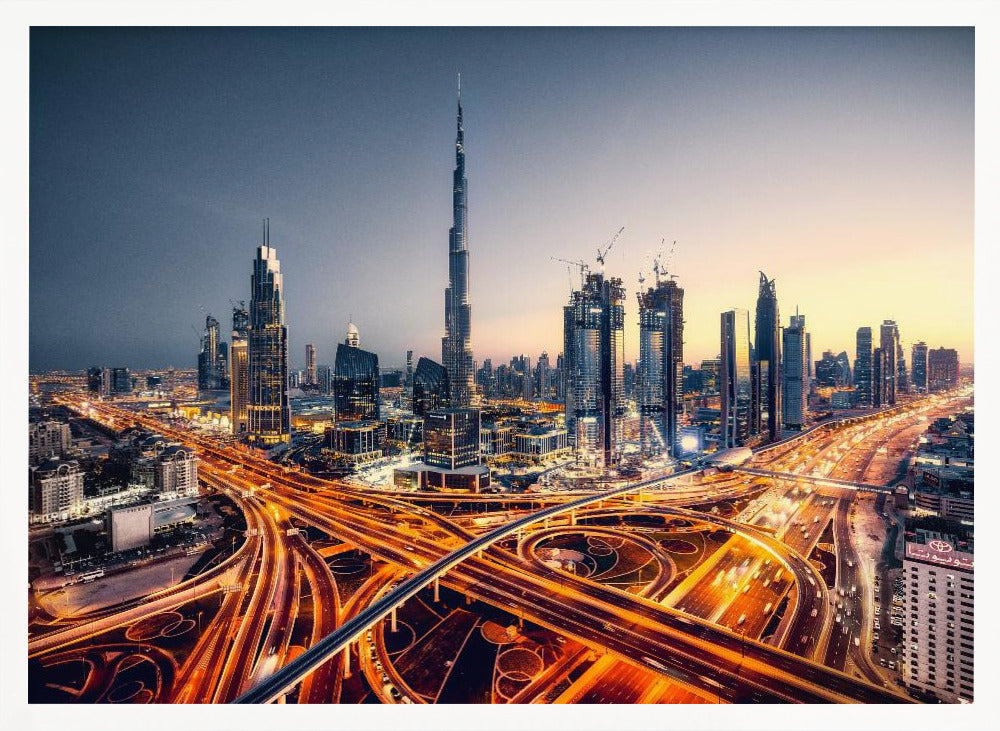 A wide-angle, elevated photograph of the Dubai skyline at dusk, with the iconic Burj Khalifa towering in the center. In the foreground, a complex network of highways glows with the orange light trails of moving traffic, while the city's numerous skyscrapers are illuminated against a twilight sky. Print