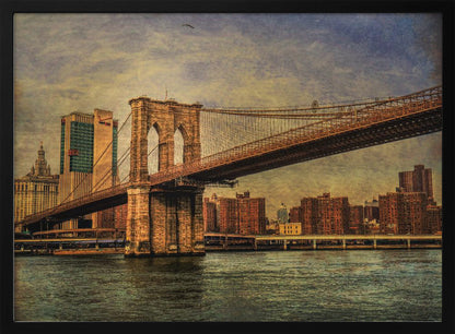 A framed, vintage-style photograph of the Brooklyn Bridge from a low angle, showing its stone pylon and suspension cables against a textured, cloudy sky. The Manhattan skyline and the East River are visible in the background and foreground. Wall Art