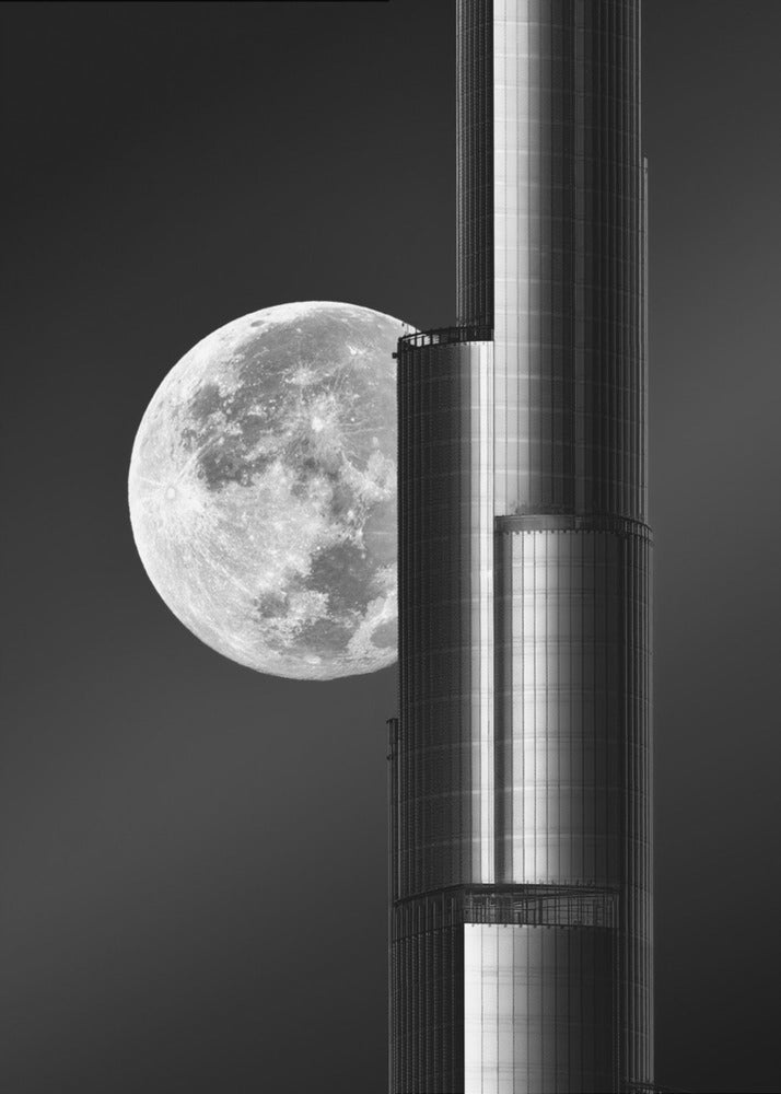 A dramatic black and white photograph of a massive full moon positioned next to a modern, towering skyscraper. The high-contrast image creates a striking juxtaposition between the natural celestial body and the man-made architectural marvel against a dark night sky. Poster