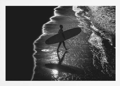 A dramatic, high-contrast, black and white aerial view of a silhouetted surfer carrying their surfboard along the shoreline. The sun glints off the wet sand and the dark water, creating a sparkling effect and a clear reflection of the surfer. Poster