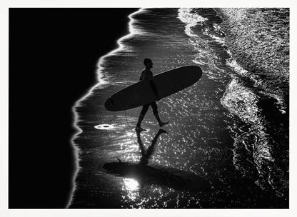 A dramatic, high-contrast, black and white aerial view of a silhouetted surfer carrying their surfboard along the shoreline. The sun glints off the wet sand and the dark water, creating a sparkling effect and a clear reflection of the surfer. Poster