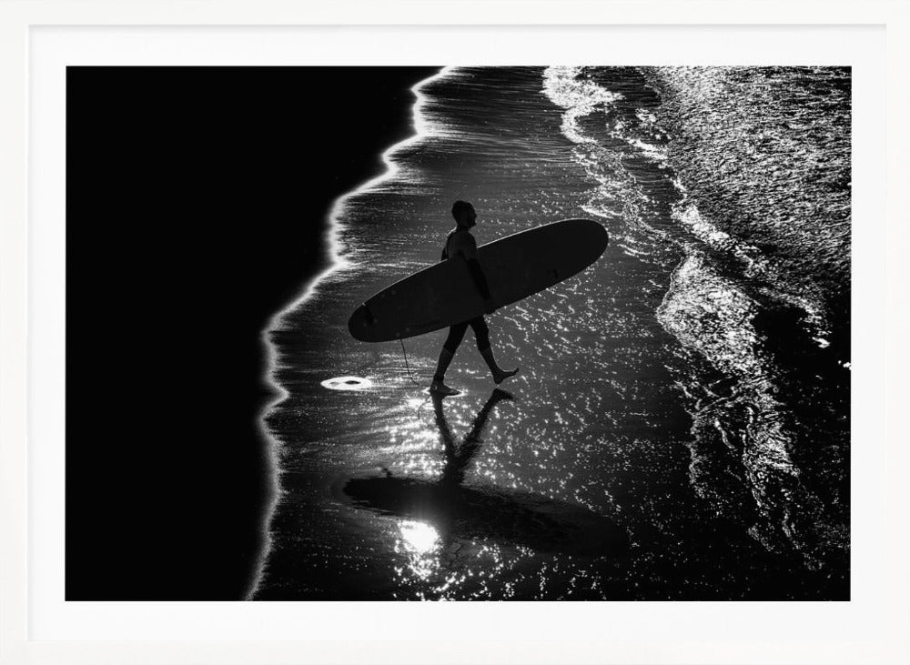 A dramatic, high-contrast, black and white aerial view of a silhouetted surfer carrying their surfboard along the shoreline. The sun glints off the wet sand and the dark water, creating a sparkling effect and a clear reflection of the surfer. Poster