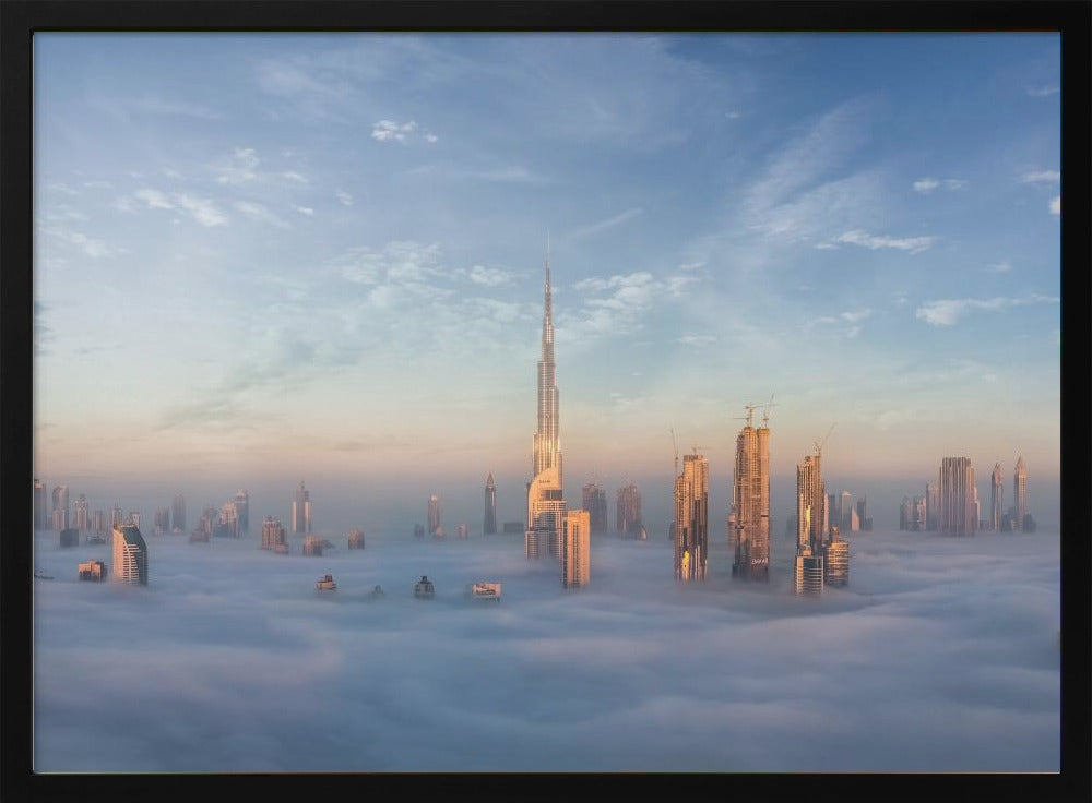 A framed photograph of the Dubai skyline, with the Burj Khalifa and other skyscrapers piercing through a thick blanket of low-lying clouds or fog. The scene is bathed in the warm, golden light of sunrise or sunset against a pale blue sky. Poster