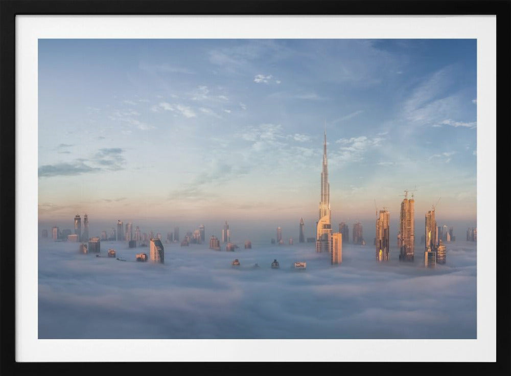 A framed photograph of the Dubai skyline, with the Burj Khalifa and other skyscrapers piercing through a thick blanket of low-lying clouds or fog. The scene is bathed in the warm, golden light of sunrise or sunset against a pale blue sky. Poster