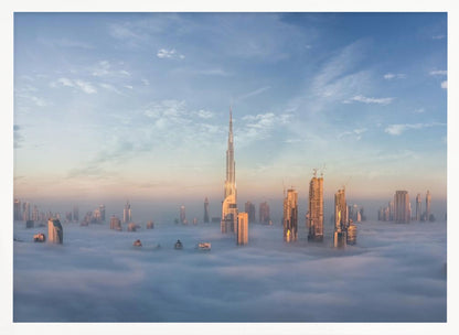 A framed photograph of the Dubai skyline, with the Burj Khalifa and other skyscrapers piercing through a thick blanket of low-lying clouds or fog. The scene is bathed in the warm, golden light of sunrise or sunset against a pale blue sky. Poster