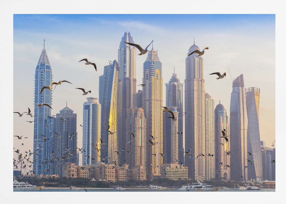 A framed artwork of the Dubai city skyline, featuring modern skyscrapers bathed in the golden light of sunset. A flock of seagulls flies in the foreground above the water, where several yachts are docked. Artwork