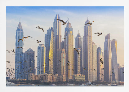 A framed artwork of the Dubai city skyline, featuring modern skyscrapers bathed in the golden light of sunset. A flock of seagulls flies in the foreground above the water, where several yachts are docked. Artwork