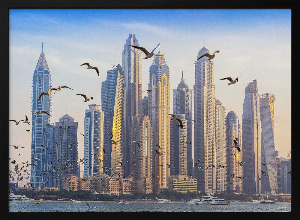 A framed artwork of the Dubai city skyline, featuring modern skyscrapers bathed in the golden light of sunset. A flock of seagulls flies in the foreground above the water, where several yachts are docked. Artwork