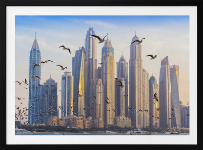 A framed artwork of the Dubai city skyline, featuring modern skyscrapers bathed in the golden light of sunset. A flock of seagulls flies in the foreground above the water, where several yachts are docked. Artwork