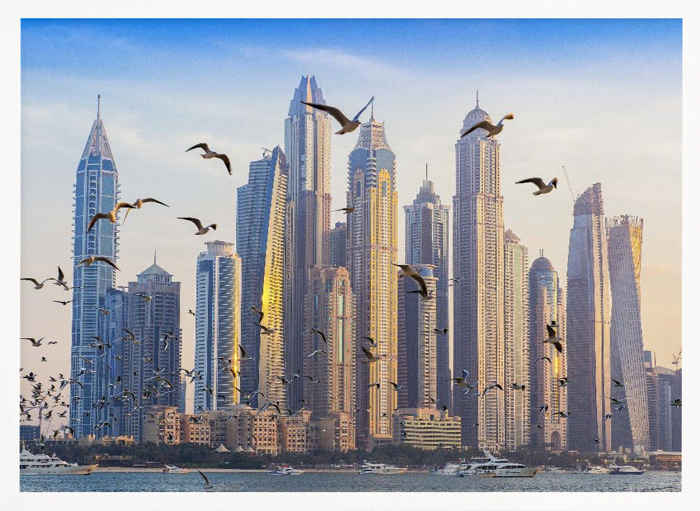 A framed artwork of the Dubai city skyline, featuring modern skyscrapers bathed in the golden light of sunset. A flock of seagulls flies in the foreground above the water, where several yachts are docked. Artwork