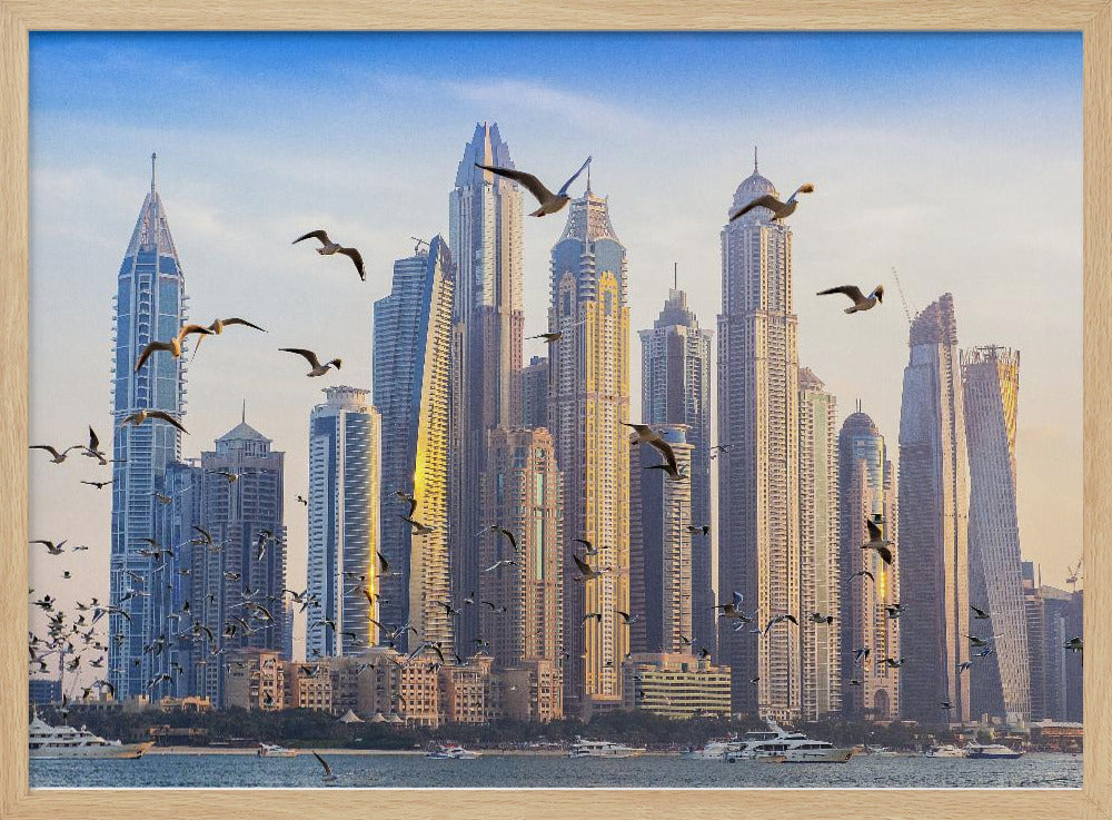 A framed artwork of the Dubai city skyline, featuring modern skyscrapers bathed in the golden light of sunset. A flock of seagulls flies in the foreground above the water, where several yachts are docked. Artwork