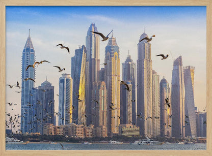 A framed artwork of the Dubai city skyline, featuring modern skyscrapers bathed in the golden light of sunset. A flock of seagulls flies in the foreground above the water, where several yachts are docked. Artwork