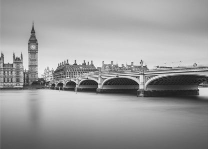 A black and white long-exposure photograph of the Elizabeth Tower (Big Ben) and the Houses of Parliament in London, viewed from across the River Thames. Westminster Bridge stretches across the frame over the smooth, milky water. The image is presented in a silver frame. Artwork