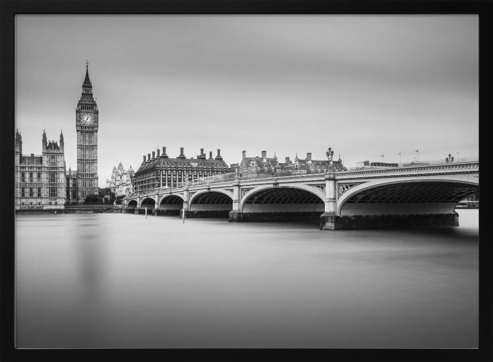 A black and white long-exposure photograph of the Elizabeth Tower (Big Ben) and the Houses of Parliament in London, viewed from across the River Thames. Westminster Bridge stretches across the frame over the smooth, milky water. The image is presented in a silver frame. Artwork