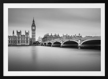 A black and white long-exposure photograph of the Elizabeth Tower (Big Ben) and the Houses of Parliament in London, viewed from across the River Thames. Westminster Bridge stretches across the frame over the smooth, milky water. The image is presented in a silver frame. Artwork