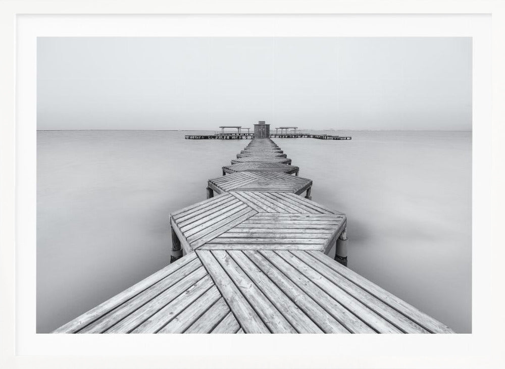 A framed, black and white photograph capturing a long wooden pier from a first-person perspective. The pier, constructed from a series of hexagonal platforms, stretches out into a calm, placid body of water that disappears into a foggy horizon, creating a serene and minimalist scene. Print